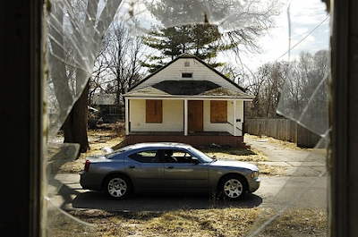 The view through an abandoned house's broken window looks out on a boarded-up house across the street on East Russell Avenue in Flint.