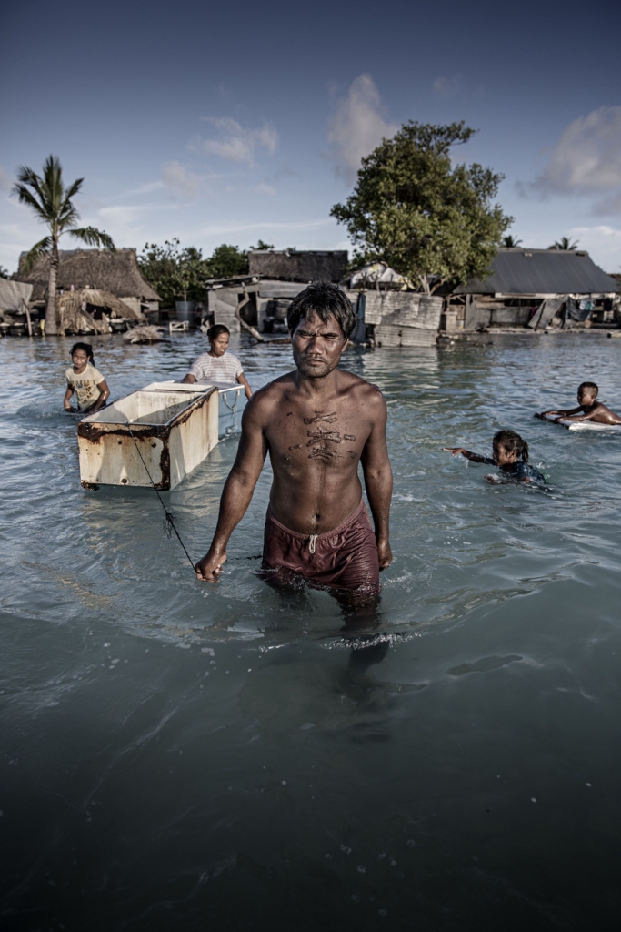 A family wades through their flooded village, floating an old fridge, collecting sea-bed stones to build a flood wall in Eita, Tarawa, Kiribati. Photo: Jonas Gratzer / LightRocket / Getty Images