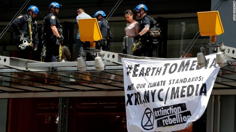 New York Police officers take into custody activists who climbed on the awning of the New York Times building to hang signs during a climate change rally, Saturday, 22 June 2019, in New York. Activists blocked traffic along 8th Avenue during a sit-in to demand coverage of climate change by the newspaper. Photo:  Julio Cortez / AP Photo