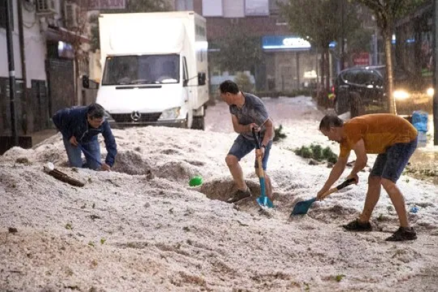 People in Madrid shovel hail after it piled up on the streets during a short, intense hail storm on 26 August 2019. Photo: EPA
