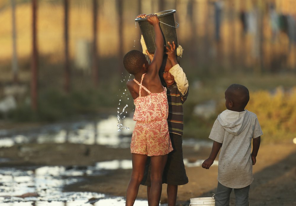 Children help each other to carry a bucket filled with water in Harare, 8 September 2019. Shortages of electricity, water, fuel, and cash are the latest symptoms of Zimbabwe’s economic decline that began in 2000 when Mugabe launched the seizures of farms owned by whites. Photo: Tsvangirayi Mukwazhi / AP Photo