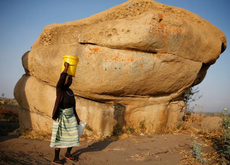 A woman carries water from an unprotected source in Mabvuku, a highly-populated suburb in Harare, Zimbabwe. Photo: Philimon Bulawayo / Reuters