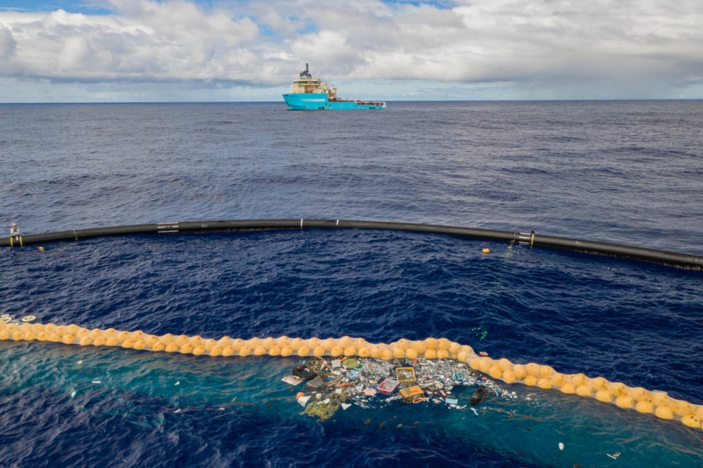 Plastic retention in front of the extended cork line, from System 001/B. The “Maersk Launcher”, which towed the assembly to the Great Pacific Garbage Patch, observes from a distance. Photo: The Ocean Cleanup