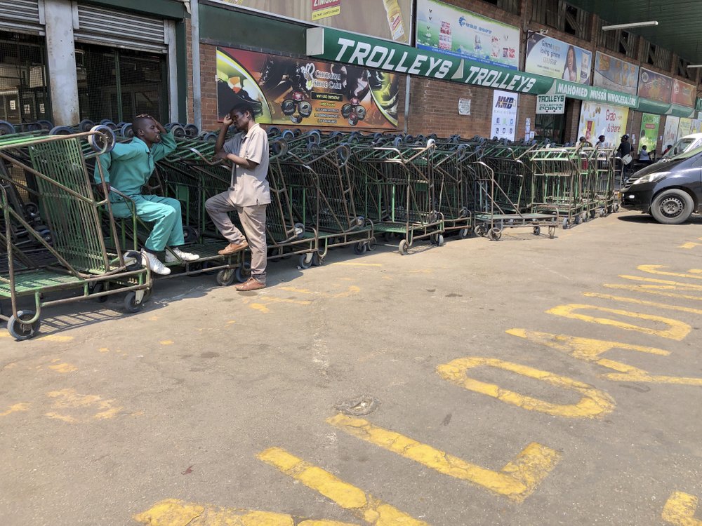 Vendors who make a living from pushing customer trollies, wait for customers outside a supermarket in Harare, on 9 October 2019. Hyperinflation is changing prices so quickly in the southern African nation that what you would see displayed on a supermarket shelf might change by the time you reach the checkout. Photo: Tsvangirayi Mukwazhi / AP Photo