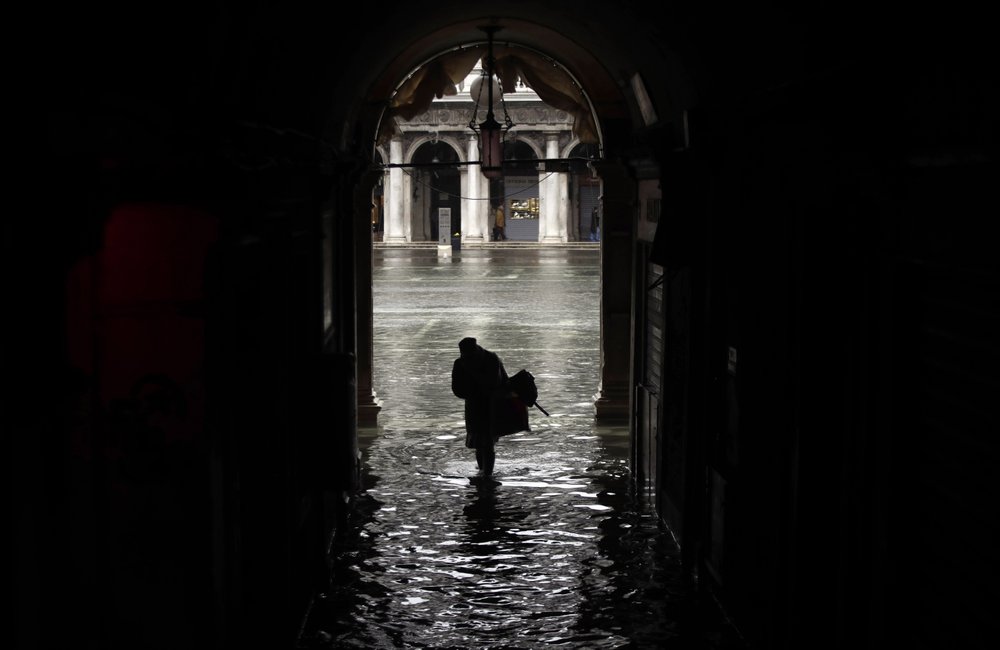 A woman is silhouetted as she walks toward a flooded St. Mark’s Square, during historic flooding in Venice, Italy, 12 November 2019. Photo: Luca Bruno / AP Photo