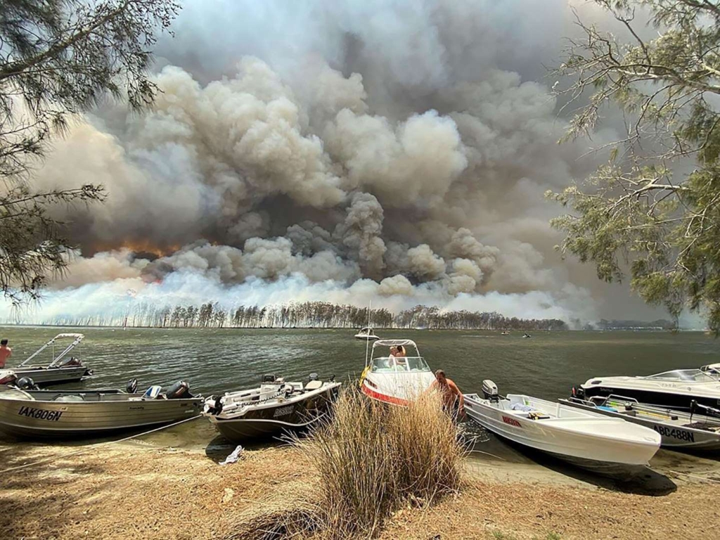Boats are pulled ashore as smoke and wildfires rage behind Lake Conjola, Australia, on Thursday, 2 January 2020. Photo: Robert Oerlemans / AP
