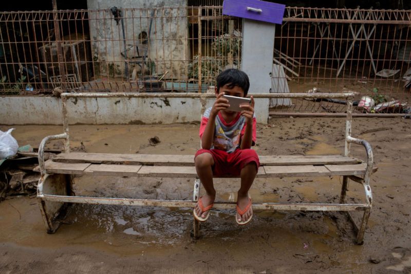 A boy plays on a phone after the flood in Bekasi, Indonesia, on 3 January 2020. Photo: Sijori Images / Barcroft Media / Getty Images
