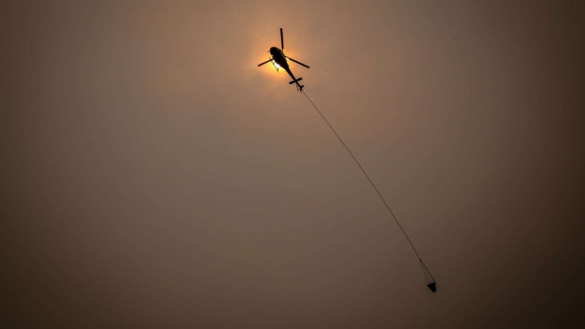 A helicopter carries water through smoky skies as it flies near the town of Bilpin, located west of Sydney in New South Wales, Australia, on Sunday, 29 December 2019. Photo: Bloomberg