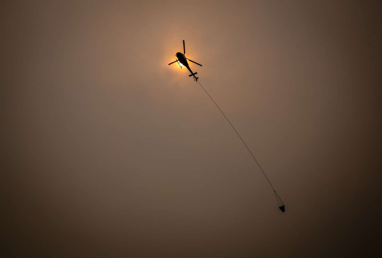 A helicopter carries water through smoky skies as it flies near the town of Bilpin, located west of Sydney in New South Wales, Australia, on Sunday, 29 December 2019. Photo: Bloomberg