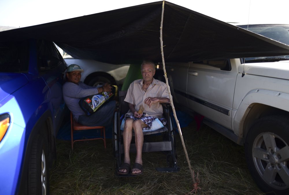 Residents from the Indios neighborhood of Guayanilla, Puerto Rico, Milagros Figueroa and Ruben Fantausi, sit under a tarp between vehicles parked on a private hay farm where locals affected by earthquakes have set up shelter amid aftershocks in Guayanilla, Puerto Rico, 10 January 2020. A 6.4 magnitude quake that toppled or damaged hundreds of homes in southwestern Puerto Rico is raising concerns about where displaced families will live, while the island still struggles to rebuild from Hurricane Maria two years ago. Photo: Carlos Giusti / AP Photo