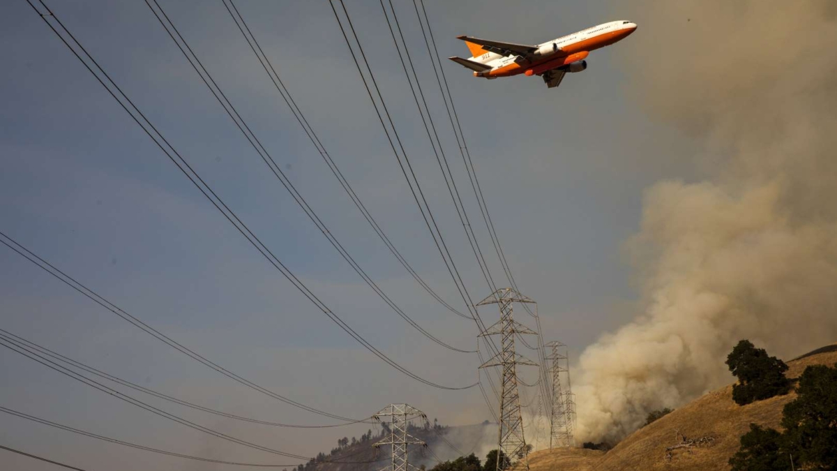 An air tanker flies over PG&E power lines en route to drop fire retardant in the valley below during the firefighting operations to battle the Kincade Fire in Healdsburg, California on 26 October 2019. Photo: Philip Pacheco / AFP / Getty Images