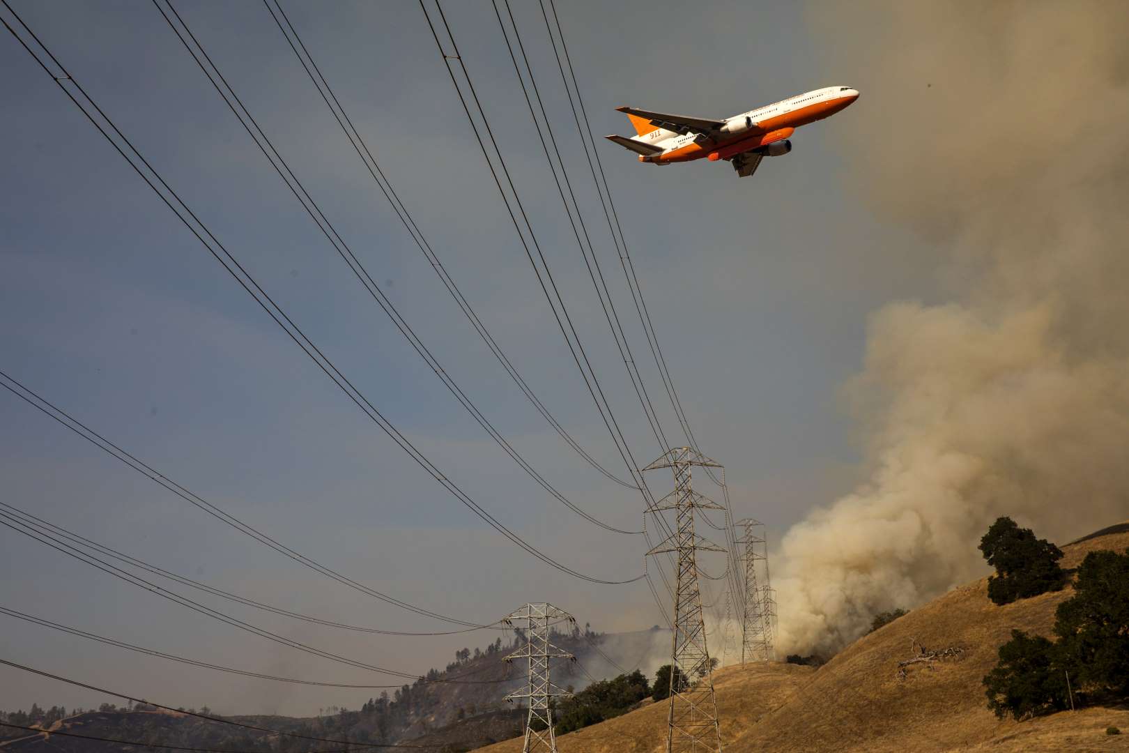 An air tanker flies over PG&E power lines en route to drop fire retardant in the valley below during the firefighting operations to battle the Kincade Fire in Healdsburg, California on 26 October 2019. Photo: Philip Pacheco / AFP / Getty Images