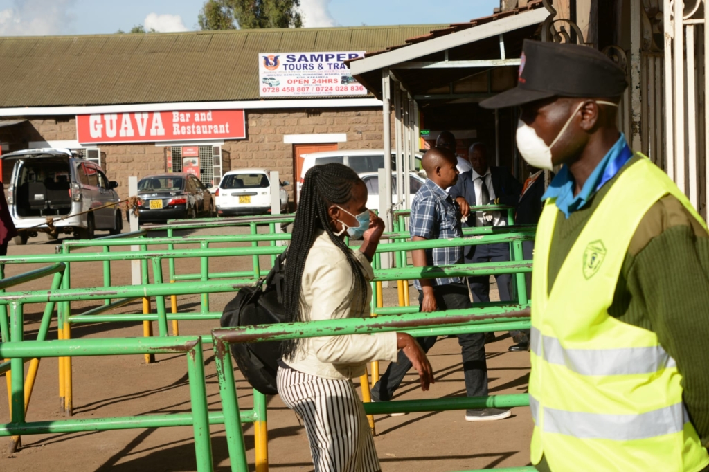 Commuters make their way into the Nairobi Train Station as a security personnel stands on guard while wearing a face mask as a preventive measure against COVID-19, 18 March 2020. Kenya has so far recorded seven case of Coronavirus. Photo: Dennis Sigwe / SOPA Images