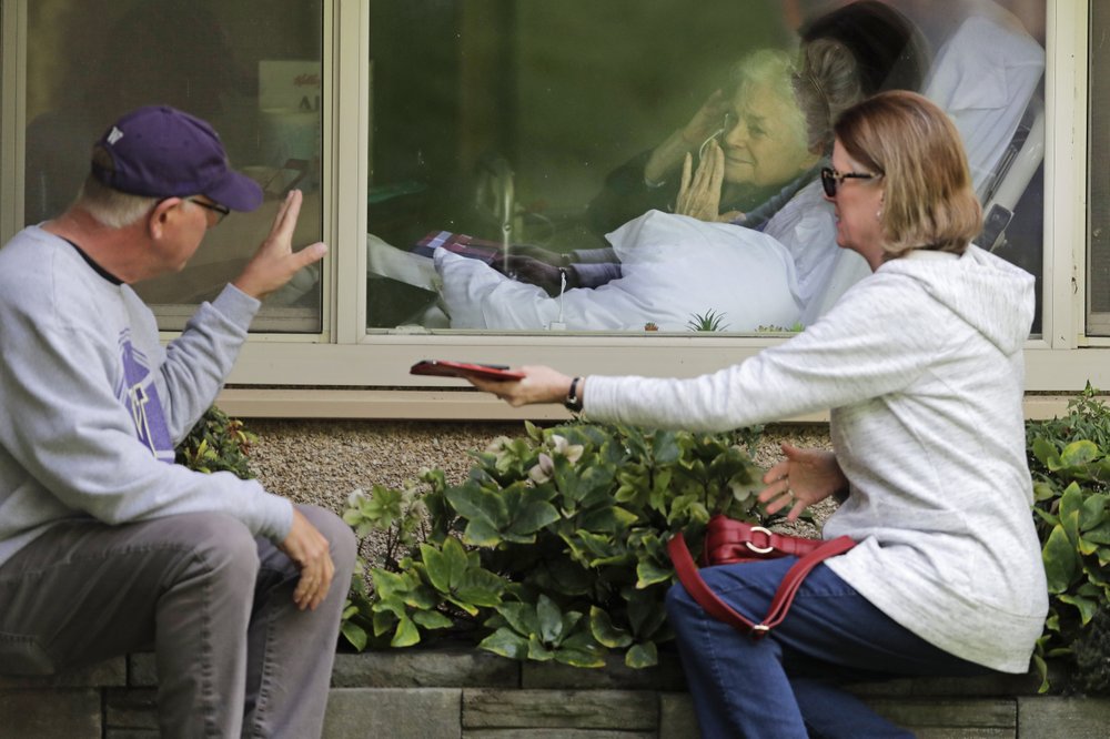 Judie Shape, center, who has tested positive for the coronavirus, blows a kiss to her son-in-law, Michael Spencer, left, as Shape's daughter, Lori Spencer, right, looks on, Wednesday, 11 March 2020, as they visit on the phone and look at each other through a window at the Life Care Center in Kirkland, Wash., near Seattle. In-person visits are not allowed at the nursing home. The vast majority of people recover from the new coronavirus. According to the World Health Organization, most people recover in about two to six weeks, depending on the severity of the illness. Photo: Ted S. Warren / AP Photo
