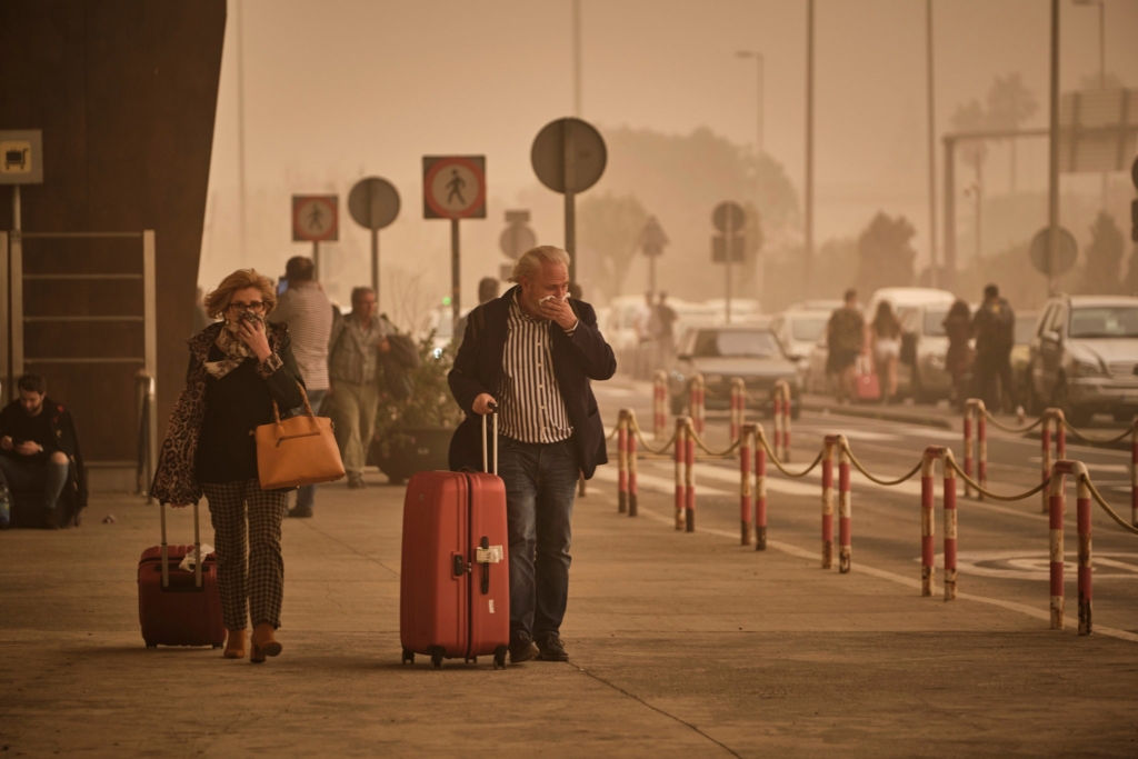 Travellers at the airport in Santa Cruz de Tenerife cover their faces to block sand during the worst sandstorm in 40 years, on 23 February 2020. Photo: Andres Gutierrez / Associated Press