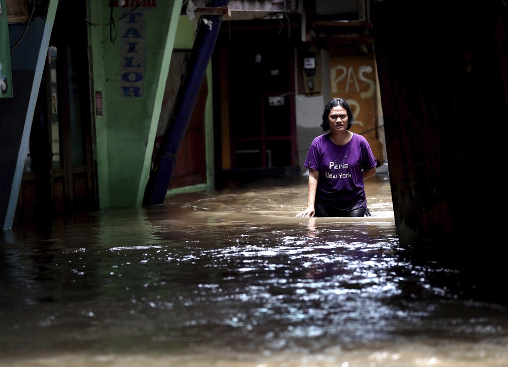 A woman wades through water in a flooded neighborhood in Jakarta, Indonesia, Tuesday, 25 February 2020. Overnight rains caused rivers to burst their banks in greater Jakarta sending muddy water into residential and commercial areas, inundating thousands of homes and paralyzing transport networks, officials said. Photo: Tatan Syuflana / AP Photo