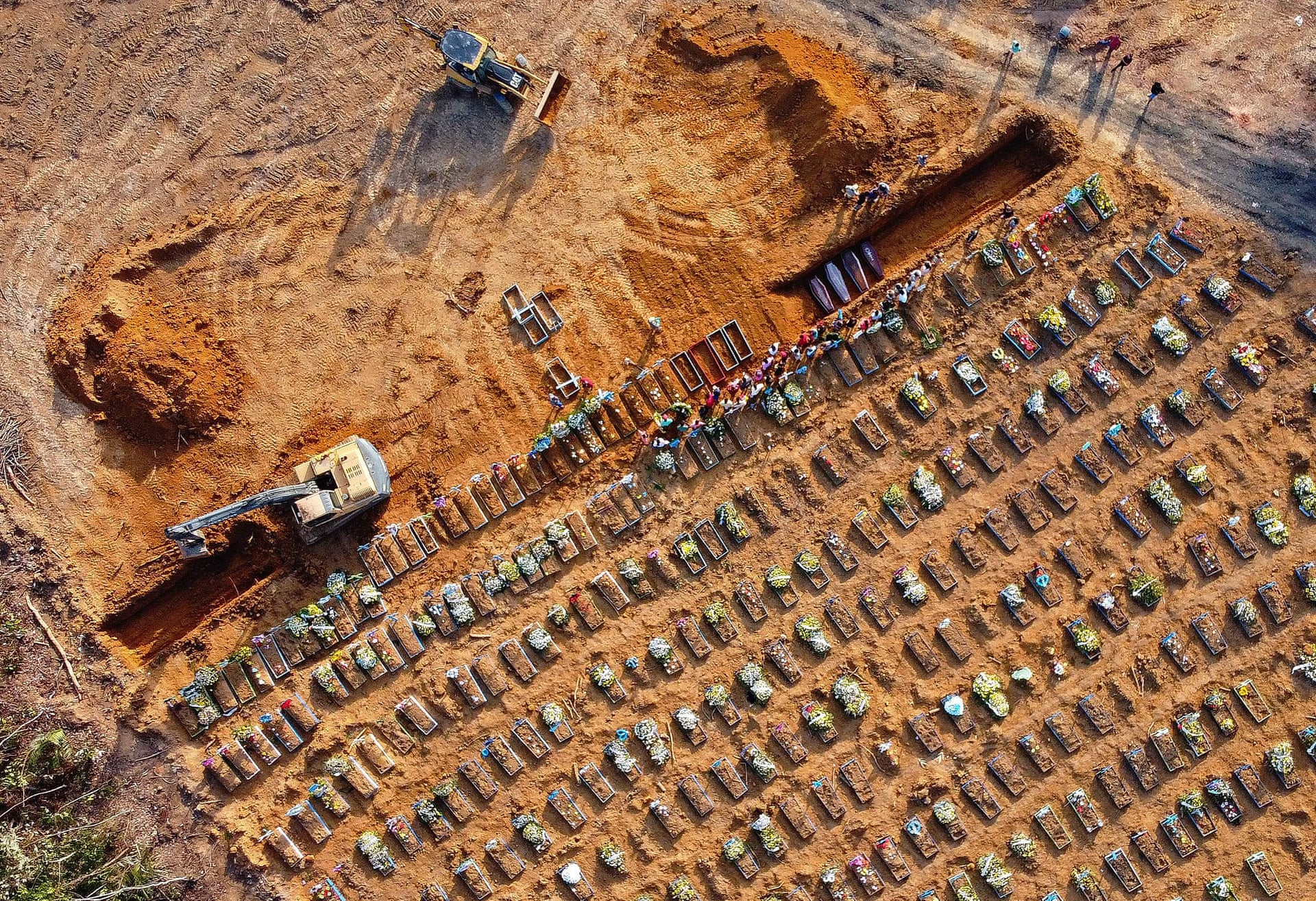 Aerial view of coffins being buried at an area where new graves have been dug at the Parque Tarumã cemetery in Manaus, Brazil, in April 2020. On 26 April 2020, 140 bodies of people killed by COVID-19 were laid to rest in Manaus, the jungle-flanked capital of Amazonas state. Normally the figure would be closer to 30 – but these are no longer normal times. Photo: Michael Dantas / AFP / Getty Images