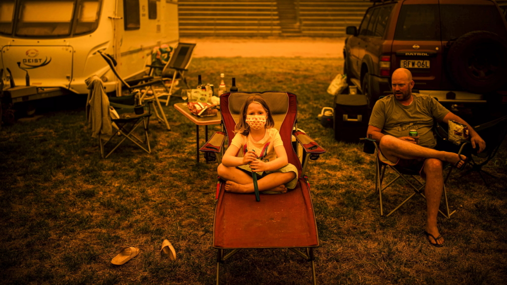 A girl wears a mask decorated with red hearts after her family fled bushfires in Australia, 31 December 2019. Thousands of vacationers and locals were forced to flee to nearly beaches in fire-ravaged southeast Australia. Blazes ripped through popular tourist areas, leaving no escape by land. Photo: Sean Davey / AFP / Getty Images