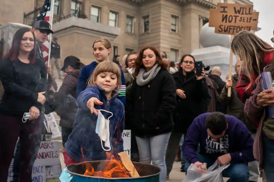 A child tosses a surgical mask into a fire during a mask-burning event at the Idaho Capitol building in Boise, Idaho on 6 March 2021. One protest sign reads, “I will not self-suffocate”. Photo: Nathan Howard / Getty Images