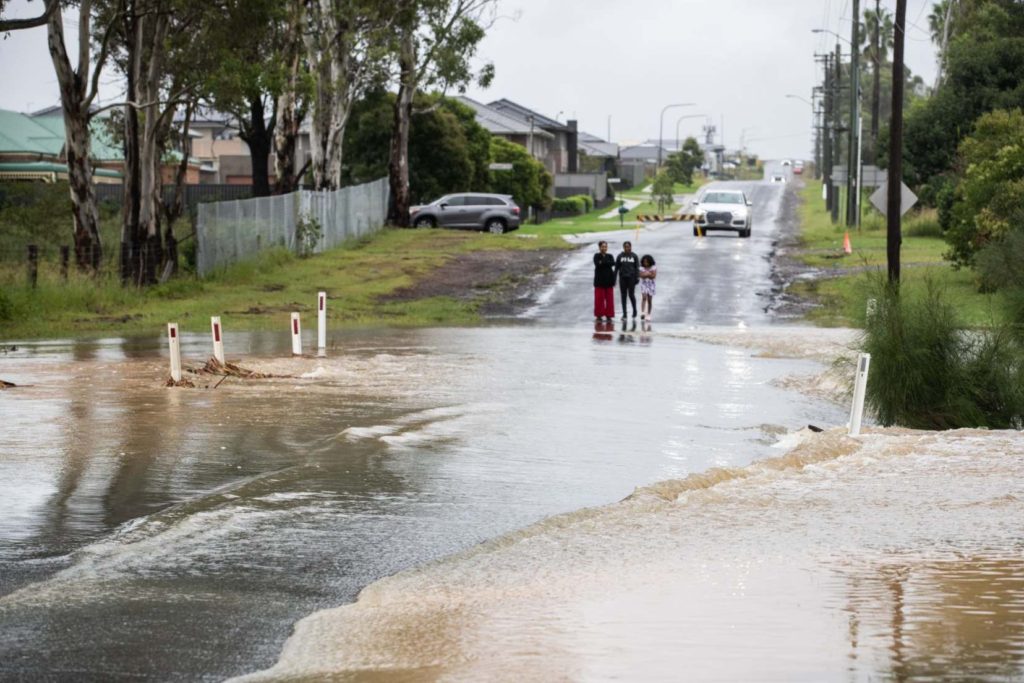 Children stand at the edge of a flooded road in the Sydney suburb of Riverstone in Australia on 21 March 2021. Photo: Edwina Pickles