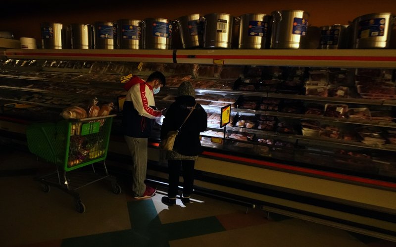 Customers use the light from a cell phone to look in the meat section of a grocery store that was without power, in Dallas, Texas,  16 February 2021. Winter Storm Uri left millions without power in Texas when the deregulated, isolated power grid went down, mostly due to natural gas supplies failing. Photo: LM Otero / AP Photo