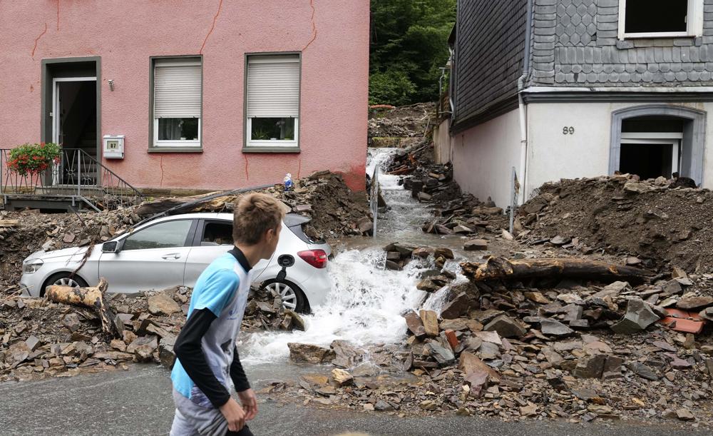 A boy walks by a car in Hagen, Germany, on 15 July 2021, that was buried in debris brought by the flooding of the 'Nahma' river the night before. At least 42 people died after record rainfall caused heavy flooding and turned streams and streets into raging torrents, sweeping away cars and causing some buildings to collapse. Photo: Martin Meissner / AP Photo