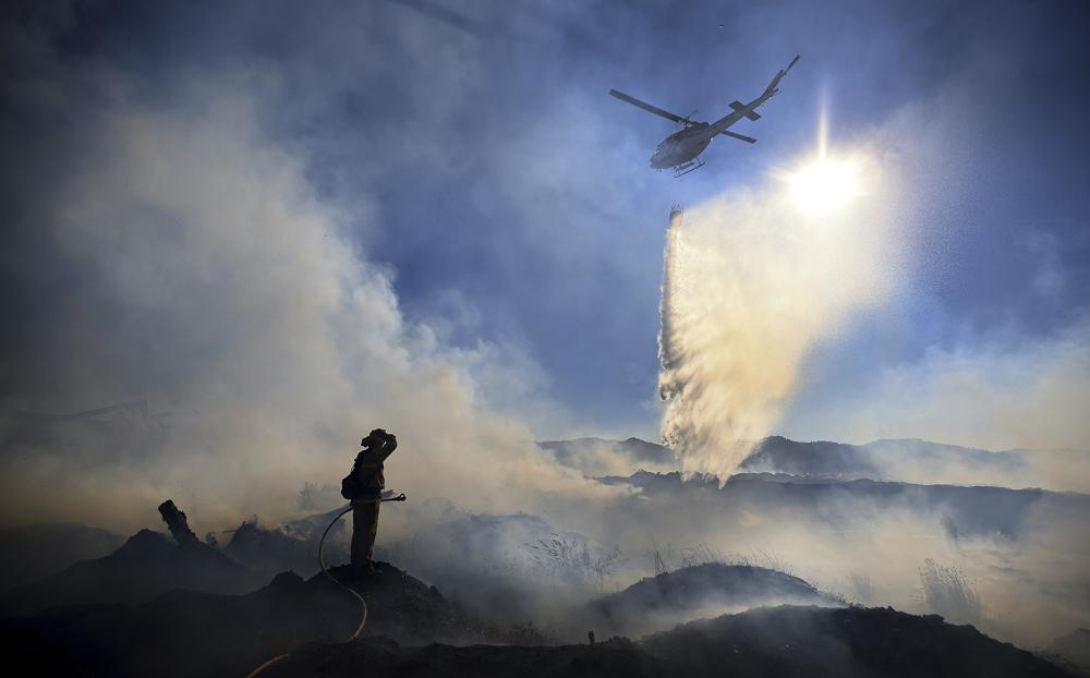 Brian Klatt, a Ukiah Valley Fire Authority firefighter, pauses as a California Department of Forestry and Fire Protection helicopter makes a drop on a brush fire that broke out next to a sawmill burning slash and large felled timber, 10 July 2021, in Ukiah, California. Photo: Kent Porter / The Press Democrat / AP