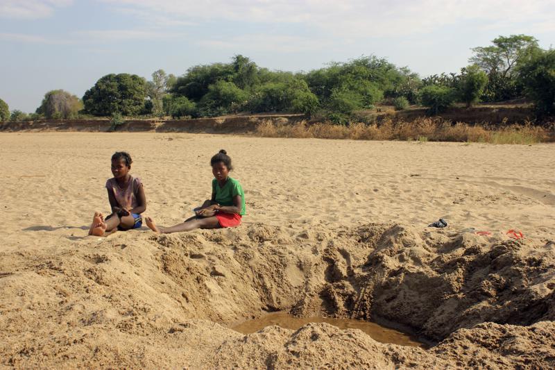 In this 11 November 2020, file photo, children sit by a dug out water hole in a dry river bed in the remote village of Fenoaivo, Madagascar. Lola Castro, WFP’s regional director in southern Africa, told a news conference Friday, 25 June 2021, that she witnessed “a very dramatic and desperate situation” during her recent visit with WFP chief David Beasley to the Indian Ocean island nation of 26 million people. Photo: Laetitia Bezain / AP Photo