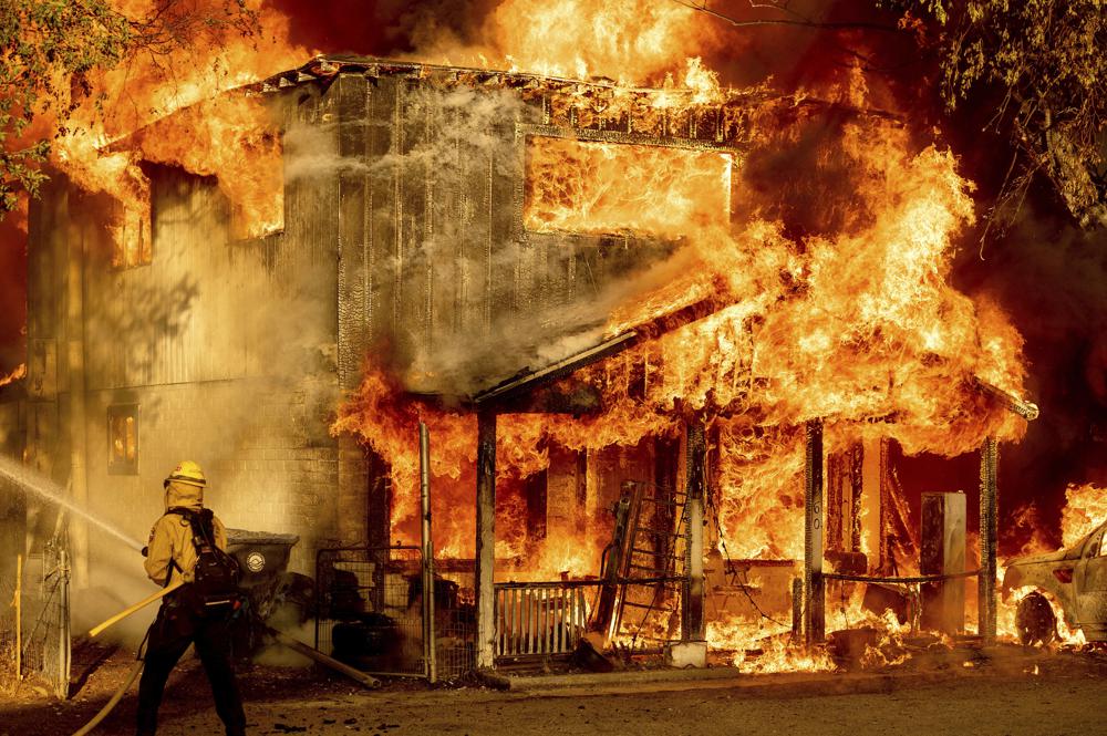 A firefighter sprays water while trying to stop the Sugar Fire, part of the Beckwourth Complex Fire, from spreading to neighboring homes in Doyle, California, on 10 July 2021. Pushed by heavy winds amid a heatwave, the fire came out of the hills and destroyed multiple residences in central Doyle. Photo: Noah Berger / AP Photo