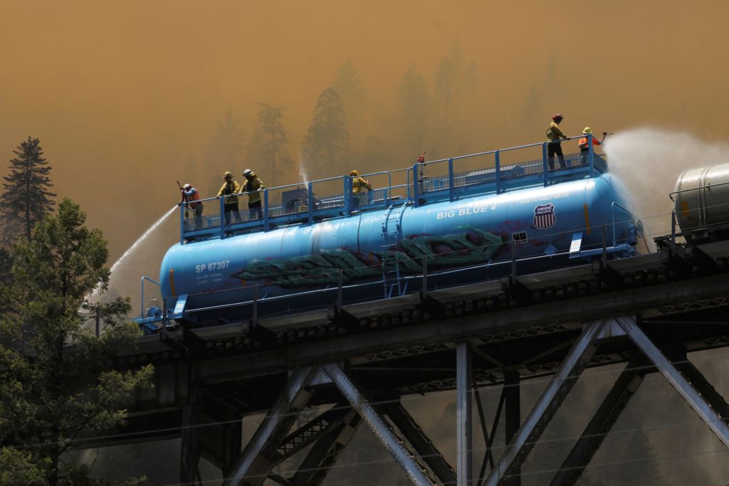 Firefighters spray water from a fire train to hot spots along the tracks over Rock Creek Bridge as the Dixie Fire grows in Plumas National Forest, California, U.S., 15 July 2021. Photo: David Swanson / REUTERS
