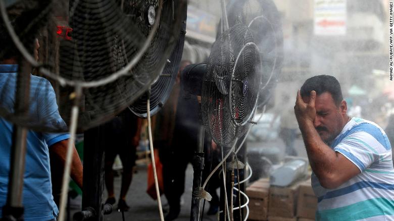 A man tries to cool down in mist sprayed from fans along a street in Baghdad, Iraq, on 30 June 2021, as temperatures surpassed 50C and the Baghdad electricity system collapsed. Photo: Ahmad Al-Rubaye / AFP / Getty Images