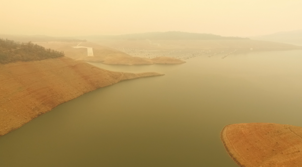 Aerial view of Lake Oroville, seen through a thick haze of smoke from California wildfires, on 20 August 2021. Boats are moored close together in the remaining water but are inaccessible, as all boat launches are closed. Photo: Action News Now