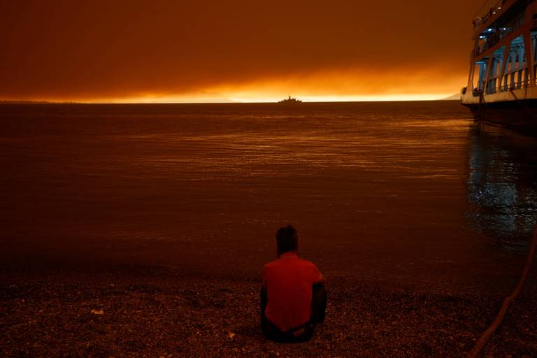 A man sits next to a ferry which used to evacuate from Pefki village on Evia island, about 189 kilometers (118 miles) north of Athens, Greece, Sunday, 8 August 2021. Pillars of billowing smoke and ash are blocking out the sun above Greece's second-largest island as a days-old wildfire devours pristine forests and triggers more evacuation alerts. Photo: Petros Karadjias / AP Photo