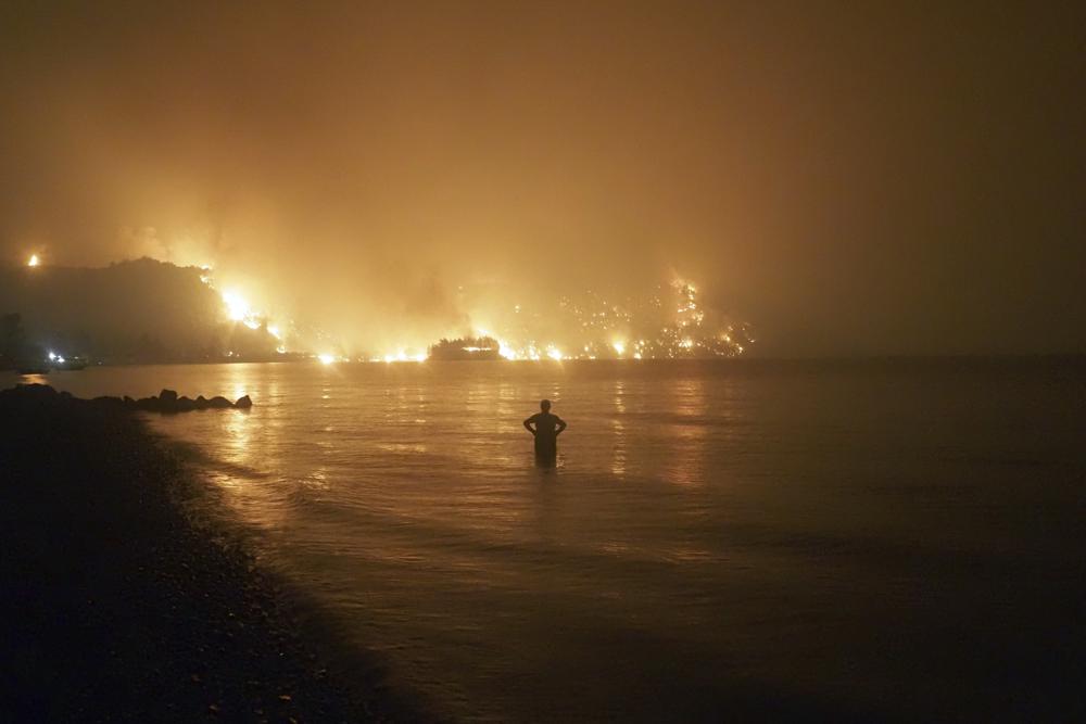 A man watches the flames as wildfire approaches Kochyli beach near Limni village on the island of Evia, about 160 kilometers (100 miles) north of Athens, Greece, late Friday, 6 August 2021. Wildfires raged uncontrolled through Greece and Turkey for yet another day Friday, forcing thousands to flee by land and sea, and killing a volunteer firefighter on the fringes of Athens in a huge forest blaze that threatened the Greek capital's most important national park. Photo: Thodoris Nikolaou / AP Photo