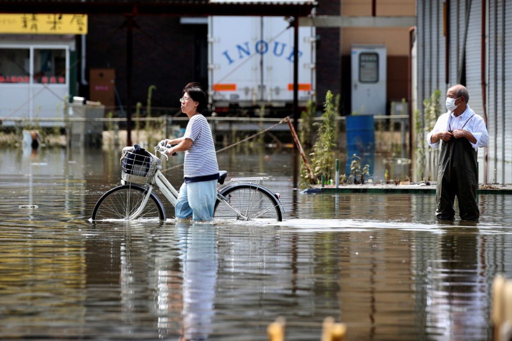 A woman pushes a bicycle through a flooded street as a man looks on, in Takeo, Saga Prefecture, western Japan, 15 August 2021. Photo: Kim Kyung-Hoon / REUTERS