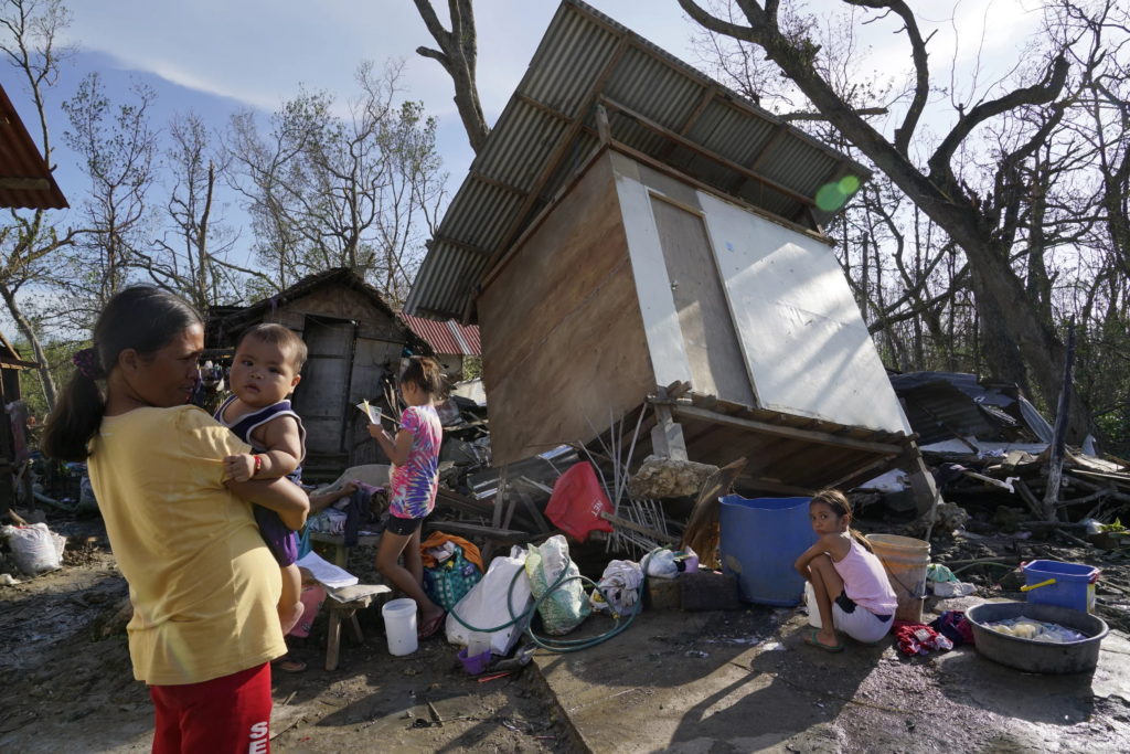 A mother and her children stand amid destroyed homes following Super Typhoon Rai in Talisay, Cebu province, central Philippines on 18 December 2021. The strong typhoon engulfed villages in floods that trapped residents on roofs, toppled trees, and knocked out power in southern and central island provinces, where more than 300,000 villagers had fled to safety before the onslaught, officials said. Photo: Jay Labra / AP