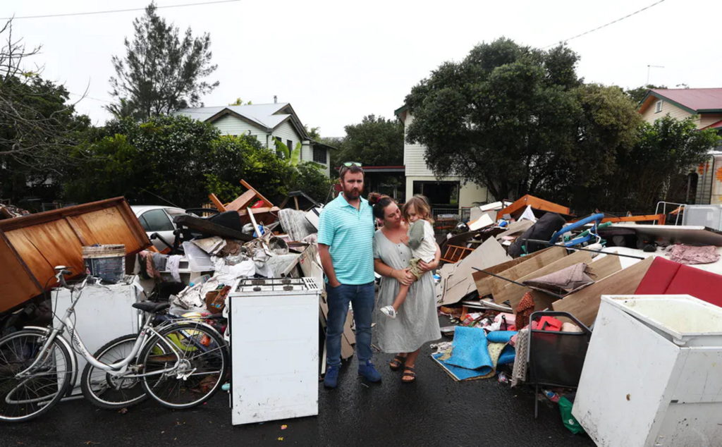 Lismore, Australia residents Tim Fry and Zara Coronakes and son Ezekiel stand outside the remains of their flooded home on 11 March 2022. Photo: Jason O'Brien / AAP