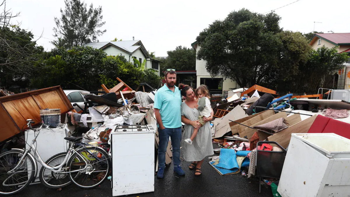 Lismore, Australia residents Tim Fry and Zara Coronakes and son Ezekiel stand outside the remains of their flooded home on 11 March 2022. Photo: Jason O'Brien / AAP