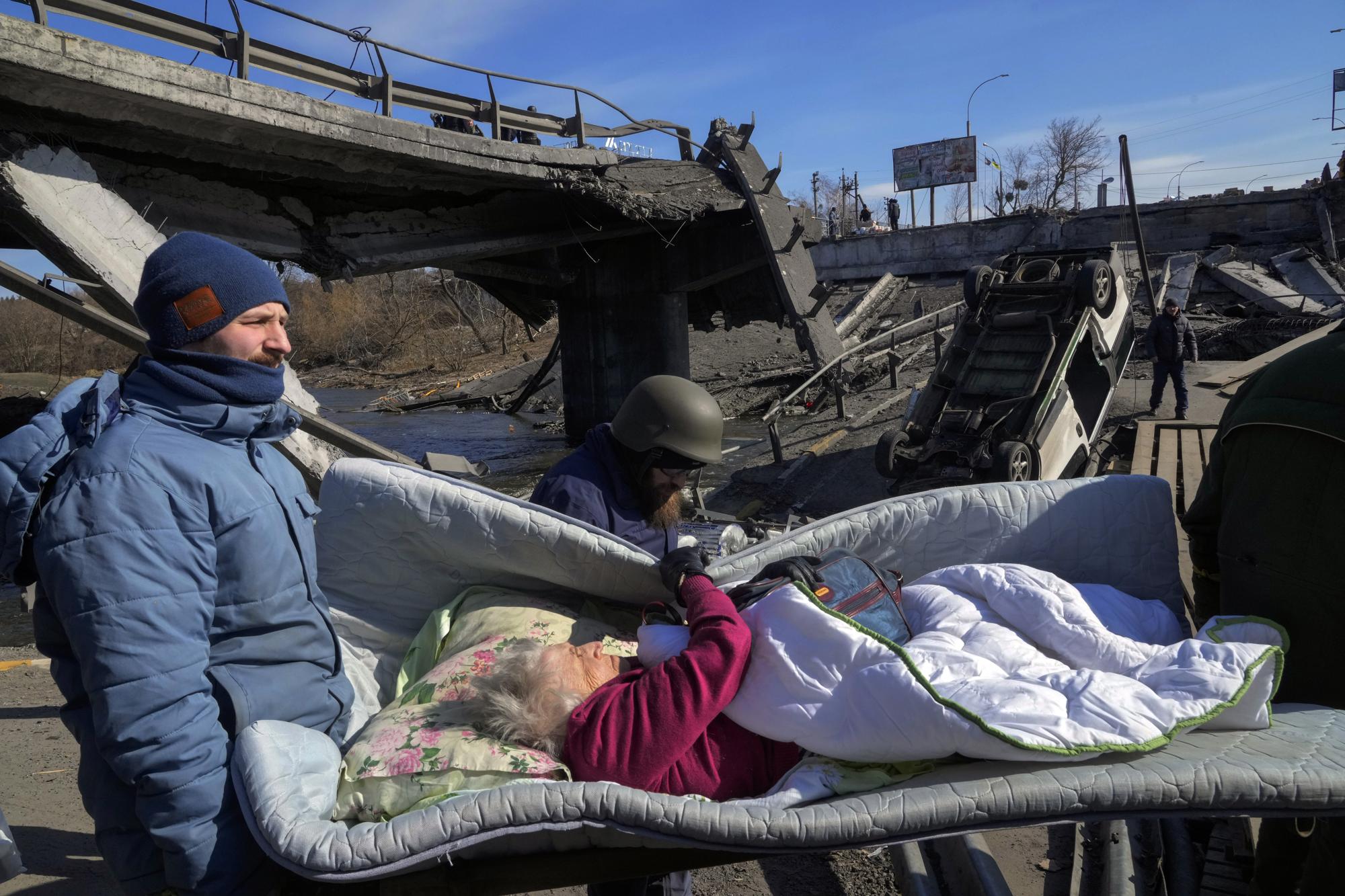 Volunteers pass an improvised path under a destroyed bridge as they evacuate an elderly resident in Irpin, northwest of Kyiv, on Friday, 11 March 2022. Photo: Efrem Lukatsky / AP Photo