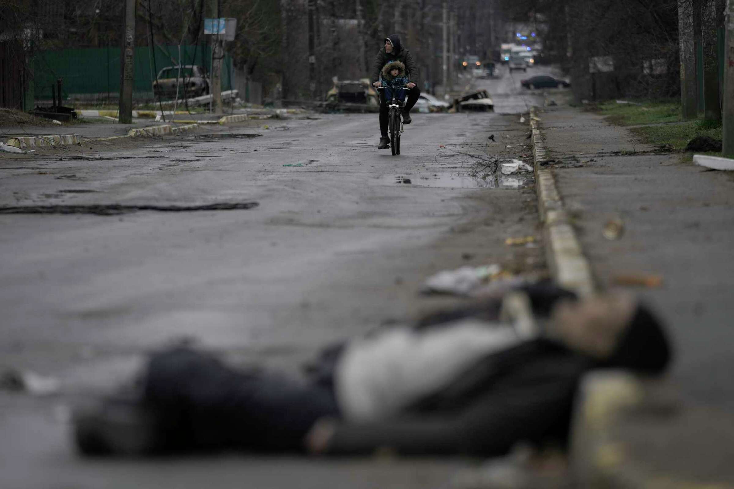 A man and child on a bicycle encounter the body of a civilian lying on a street in the formerly Russian-occupied Kyiv suburb of Bucha, Ukraine, on Saturday, 2 April 2022. Photo: Vadim Ghirda / AP