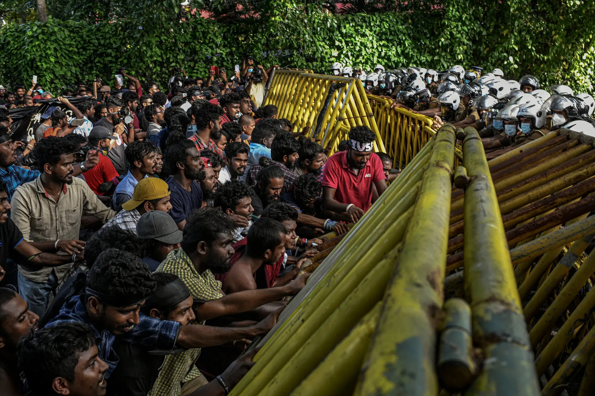 Protesters in Sri Lanka confront police across a barricade, 19 May 2022. With no end in sight to the national economic crisis that led them to take to the streets, protesters in Sri Lanka are digging in against a president they blame for crashing the economy. On 19 May 2022, as hundreds of student protesters continued their call for the resignation of President Gotabaya Rajapaksa, they were met with police tear gas and water cannons. They endured this, and a monsoon downpour that followed, adding loudspeakers to amplify their chants and speeches expressing anger at the government. Photo: Atul Loke / The New York Times