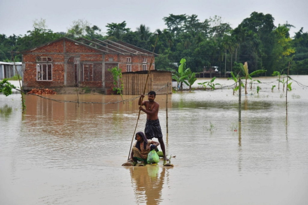 Villagers make their way on a raft past homes in a flooded area after heavy rains in Nagaon district, Assam state, India in May 2022. Photo: Biju Boro / AFP