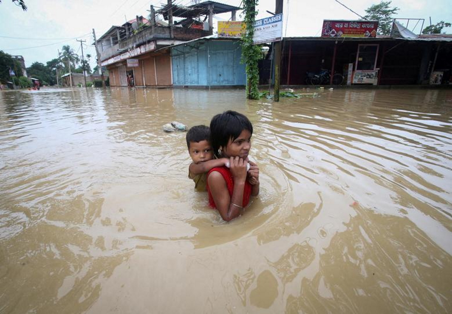 A girl carries her brother as she wades through a flooded road after heavy rains, on the outskirts of Agartala, India, 18 June 2022. Photo: Jayanta Dey / REUTERS