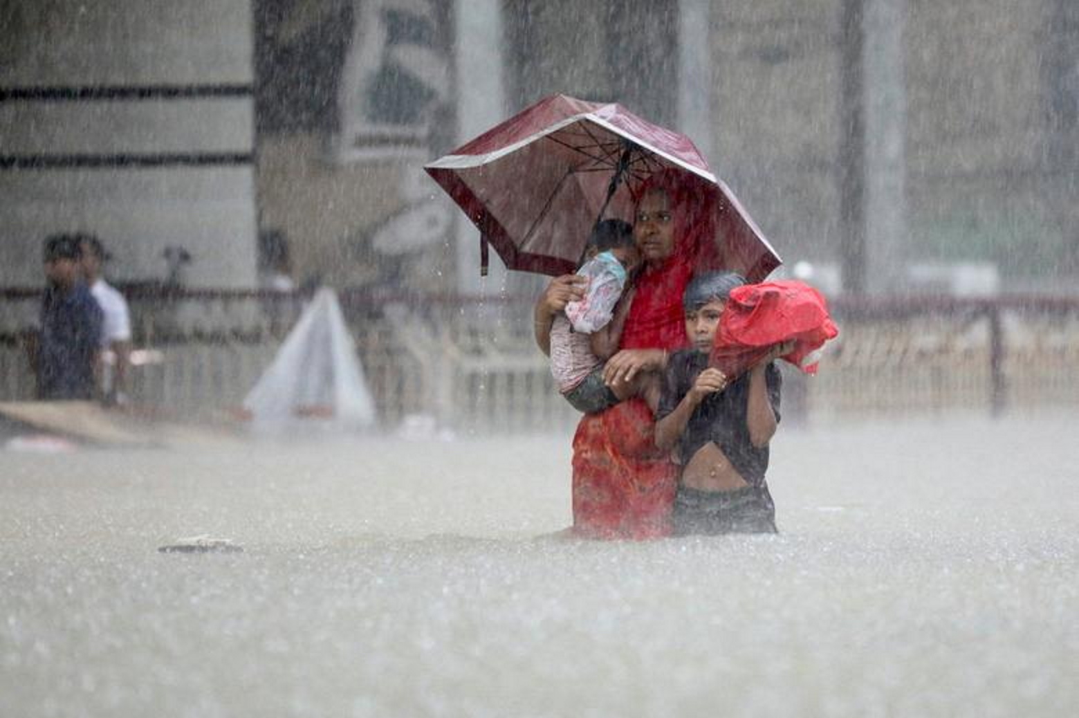 A mother and her two children wade through the water as they look for shelter during a flood, amidst heavy rains that caused widespread flooding in the northeastern part of the country, in Sylhet, Bangladesh, 18 June 2022. Photo: Abdul Goni / REUTERS