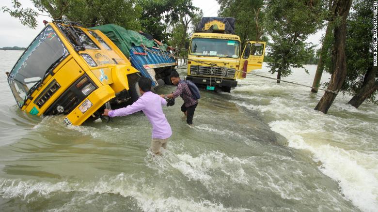 People wade past stranded trucks on a flooded street in Sunamganj, Bangladesh on 21 June 2022. Photo: Mamun Hossain / AFP / Getty Images