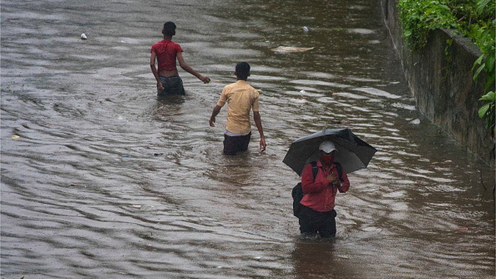 People wade through waterlogged road due to heavy rain at Tilak Nagar Station on 5 July 2022 in Mumbai, India. Photo: Getty Images