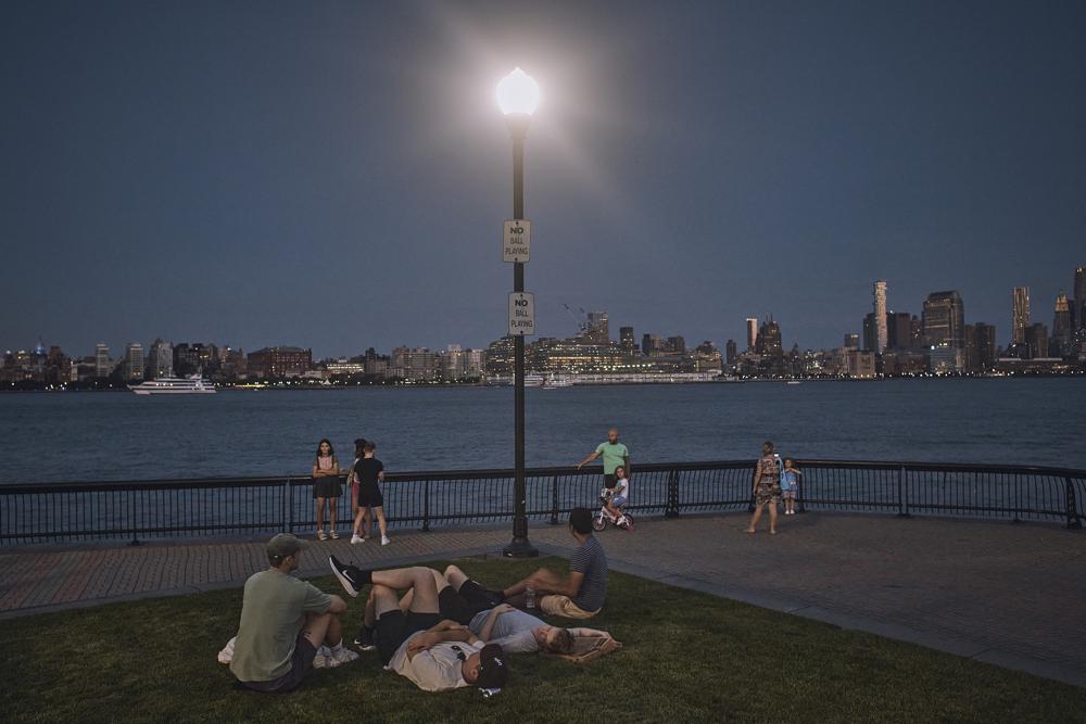 People spend time at the park at dusk during a summer heat wave, 21 July 2022, in Hoboken, N.J. The continental United States in July 2022 set a record for overnight warmth, providing little relief from the day’s sizzling heat for people, animals, plants and the electric grid, meteorologists said. Photo: Andres Kudacki / AP Photo