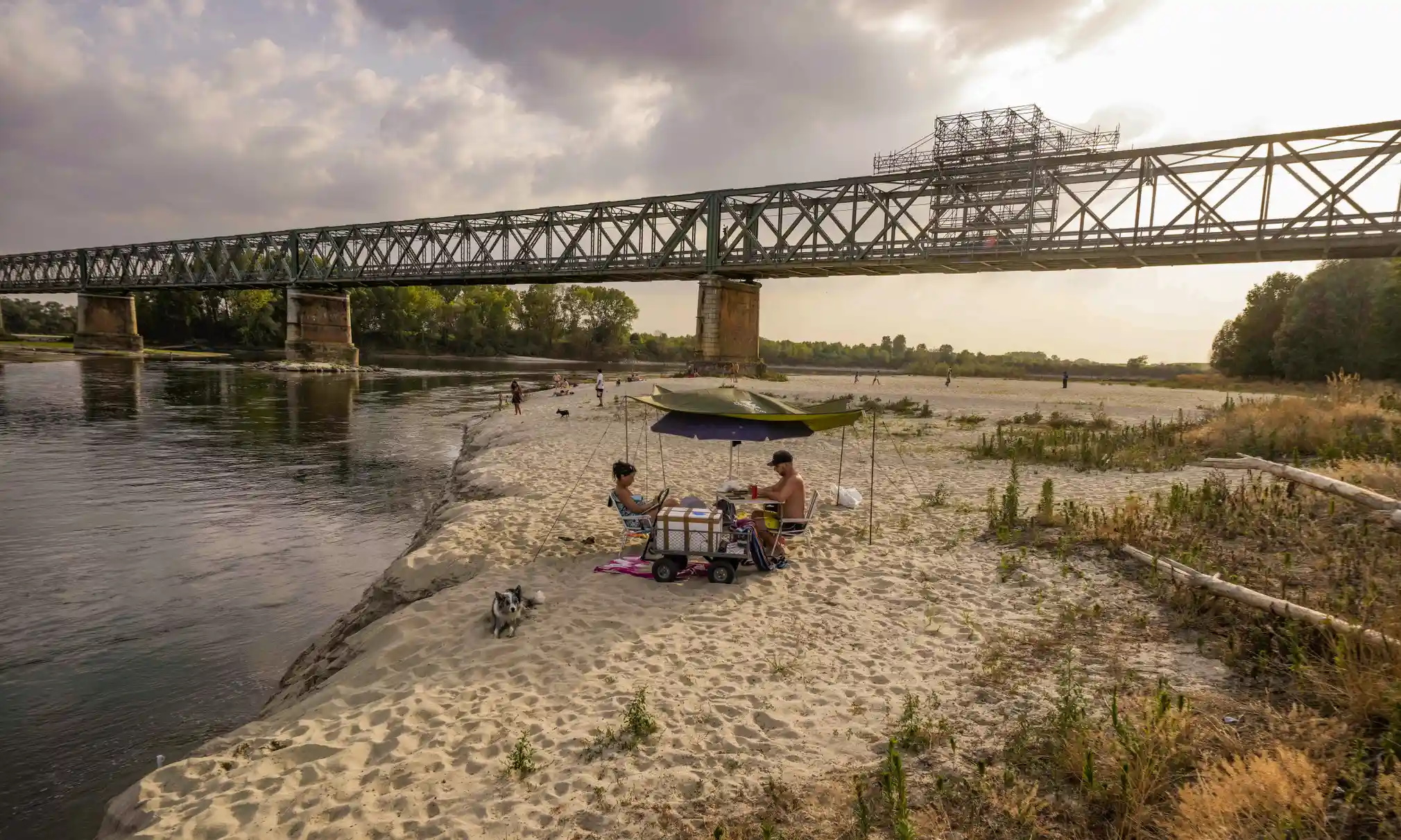 People relax at sunset on the Po riverbed next to Becca Bridge. Italy’s longest river, which is turning into a long stretch of sand due to the lack of rain, is leaving the Lomellina rice flats – nestled between the river and the Alps – without the necessary water to flood the paddies. Photo: Luca Bruno / AP