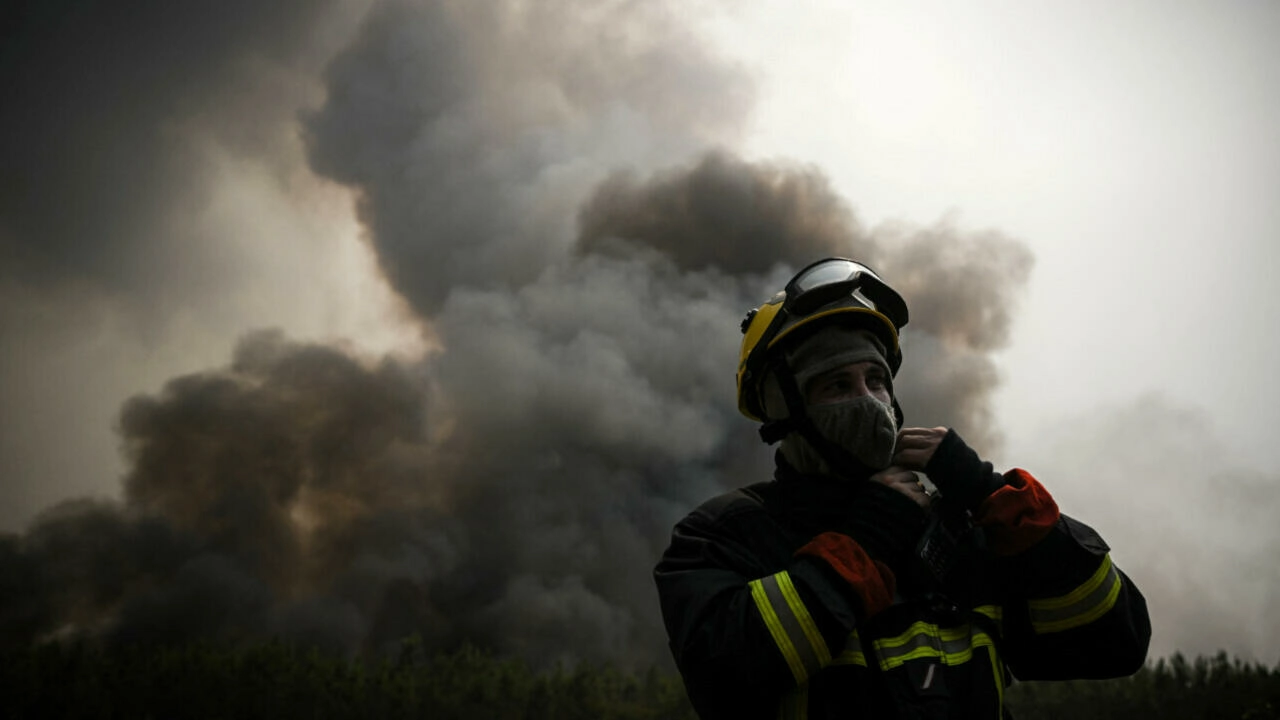 A firefighter adjusts his helmet as he stands guard to monitor a fire near Saint-Magne, southwestern France on 11 August 2022. Photo: Philippe Lopez / AFP