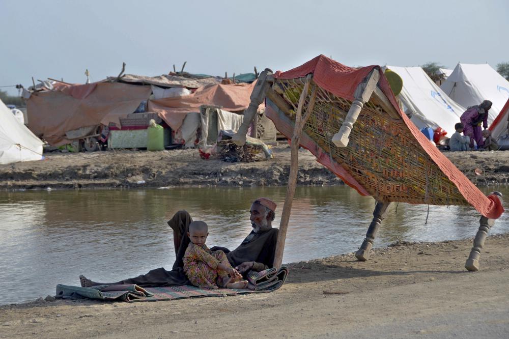 Flood victims sit under the shadow of a cot while they refuge on a roadside, in, Jaffarabad, a district of southwestern Baluchistan province, Pakistan, Monday, 17 September 2022. Photo: Zahid Hussain / AP Photo